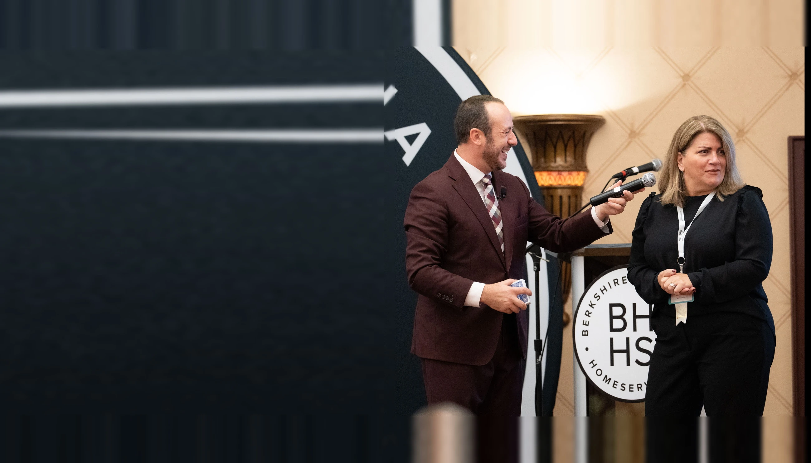 Kostya Kimlat holding a microphone out to a woman from the audience at a Berkshire Hathaway HomeServices event, both mid-conversation