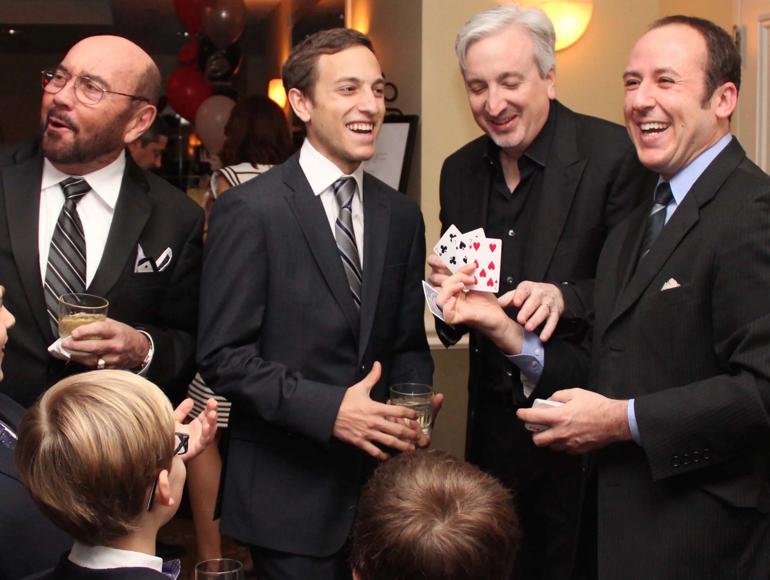 Kostya Kimlat performing close-up card magic for a small group of men in suits at an event