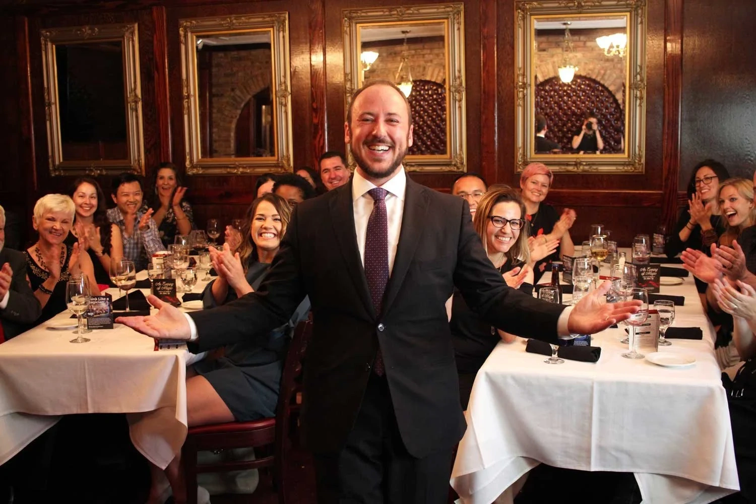 Kostya Kimlat with his arms spread wide in the wood-paneled parlor at Christner’s as the seated dinner guests around him applaud