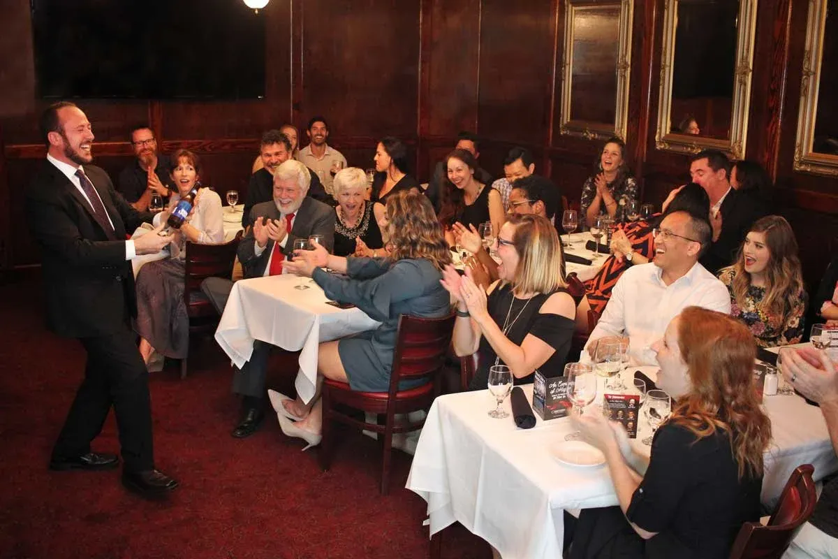A full room of dinner guests laughing and applauding as Kostya Kimlat performs beside their tables