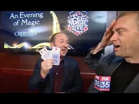 A FOX 35 News anchor reacting with his hand to his head as a See Magic Live magician fans playing cards