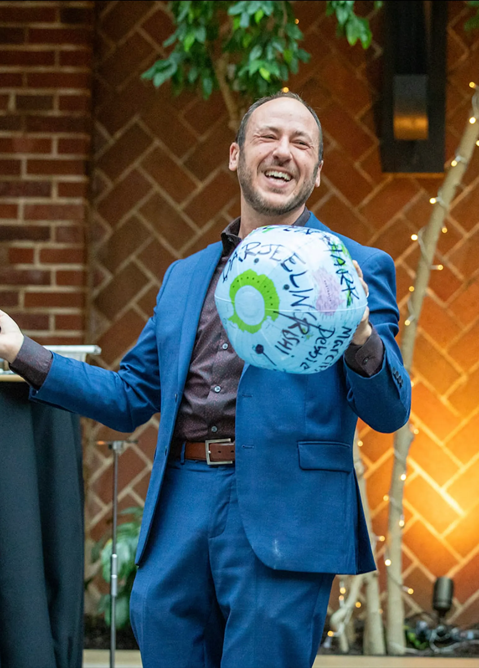 Kostya Kimlat laughing as he holds up an inflatable globe covered in handwriting, a brick courtyard wall behind him