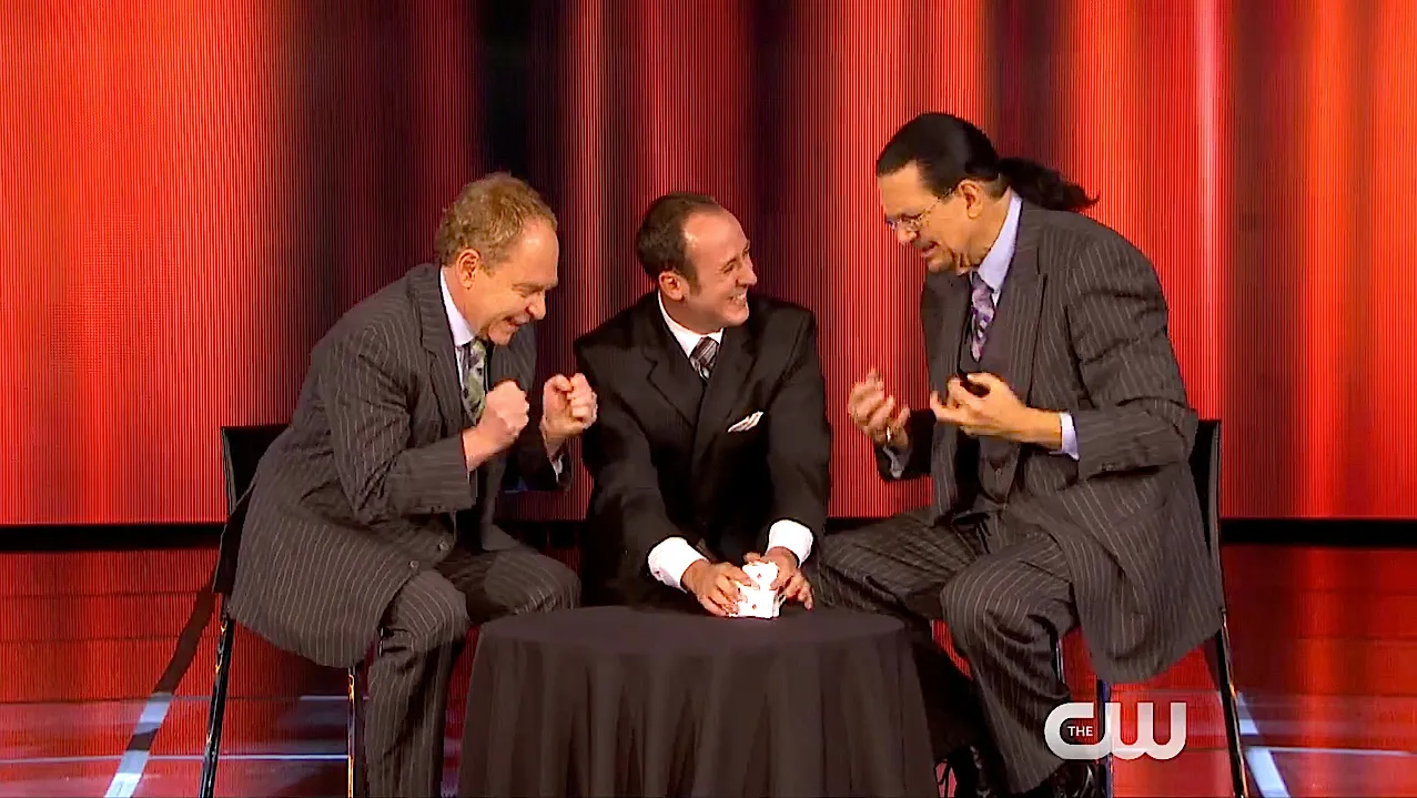 Teller and Penn Jillette react with delight as Kostya, seated between them, holds a deck of cards on Penn & Teller: Fool Us