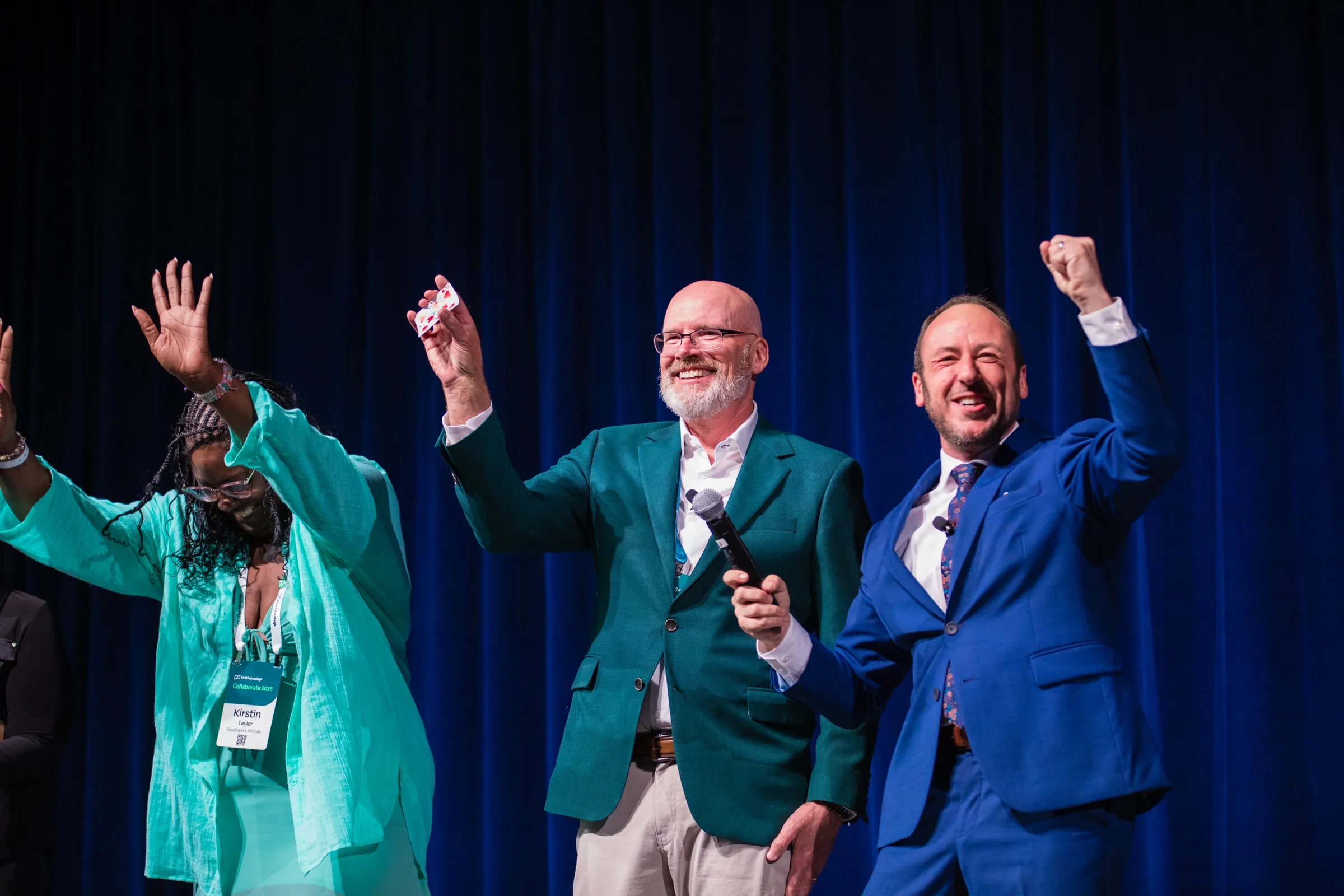 Kostya celebrates on stage with two audience volunteers, arms raised
