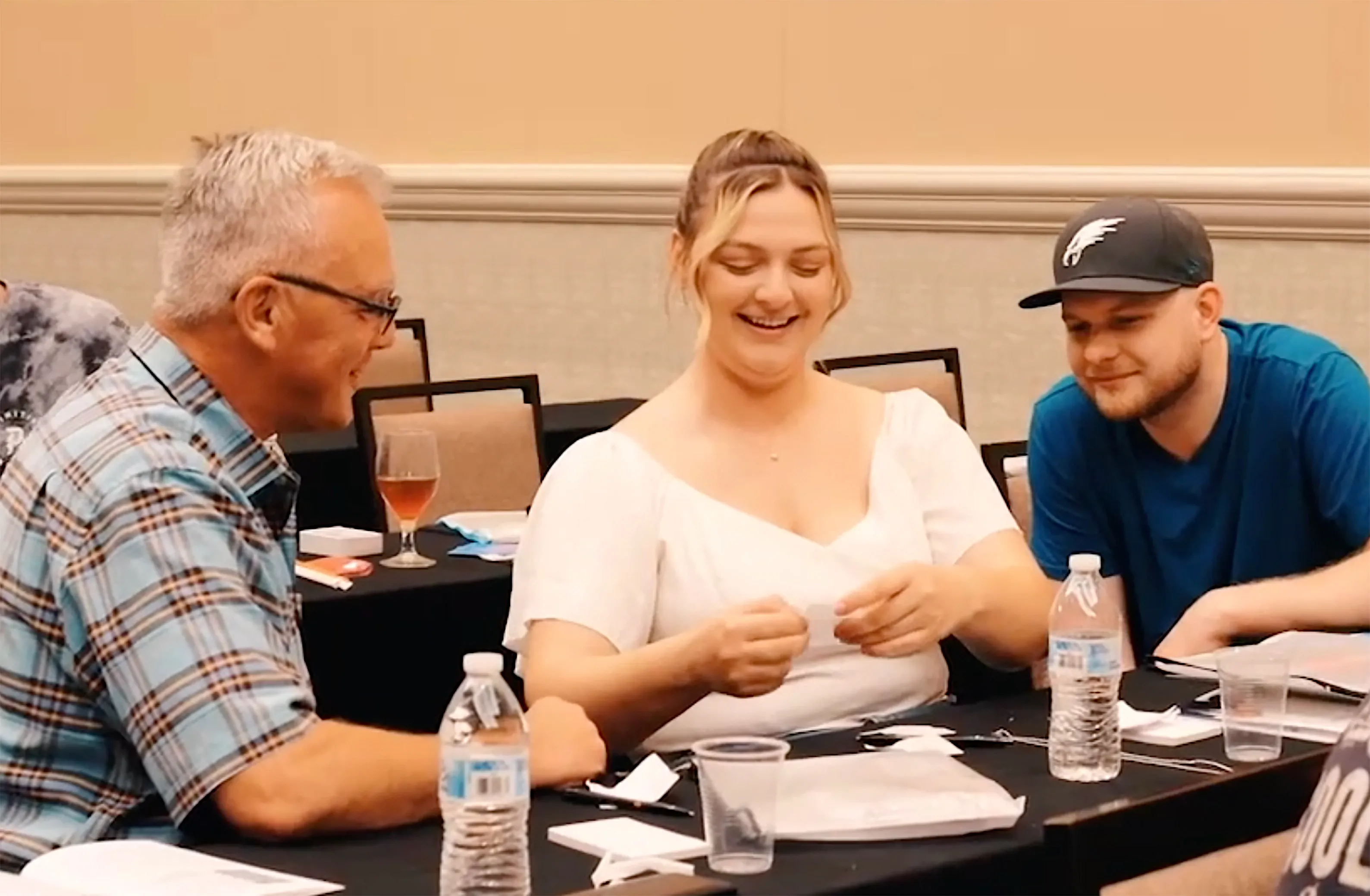 Three workshop participants at a table, the one in the middle working a folded slip of paper between her fingers while the other two watch