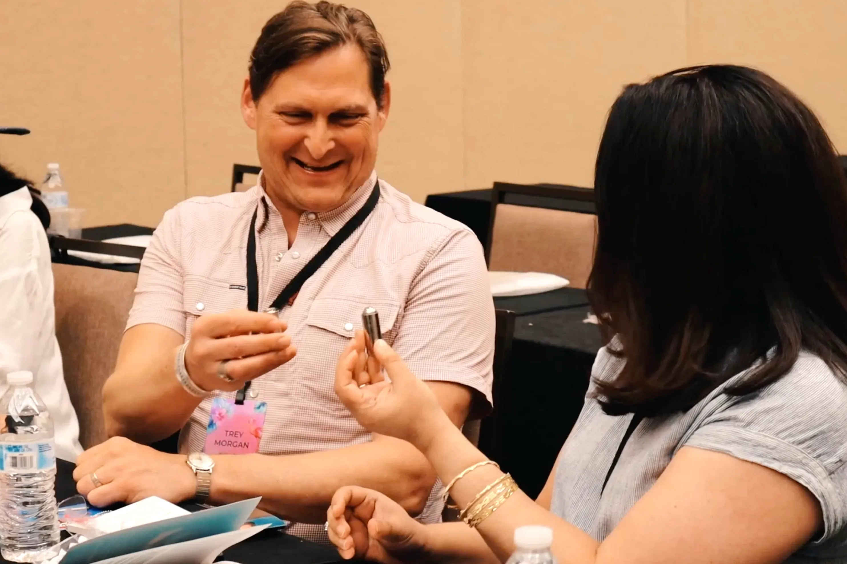 Two workshop participants laughing at a table as one holds a small metal object out to the other