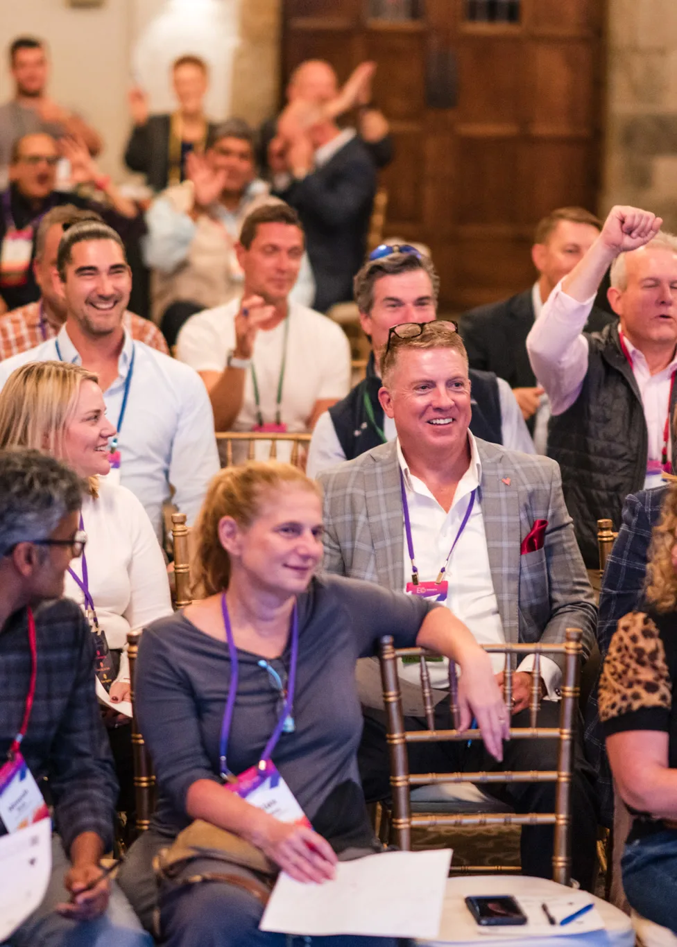 Seated attendees laughing and cheering with worksheets on their laps, one man raising his fist in the air