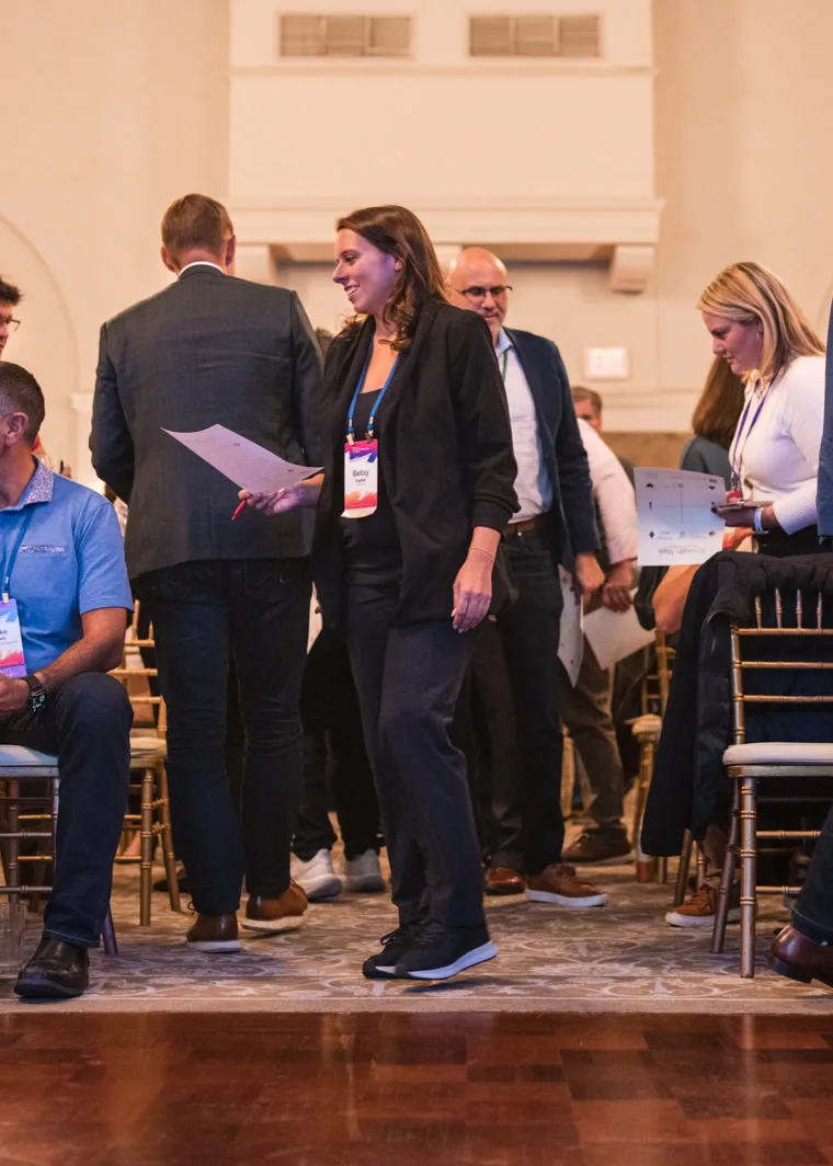 Attendees on their feet between the rows of chairs, a smiling woman in the middle walking across with her worksheet