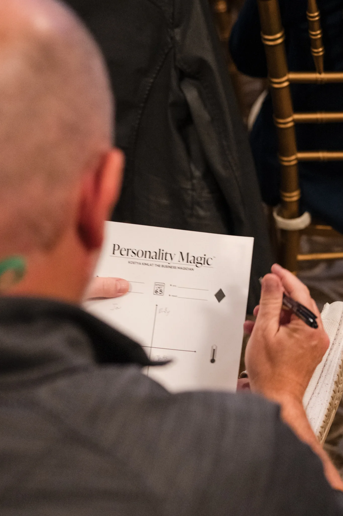 Over an attendee’s shoulder: his Personality Magic worksheet, with names written on it, and a pen in his hand
