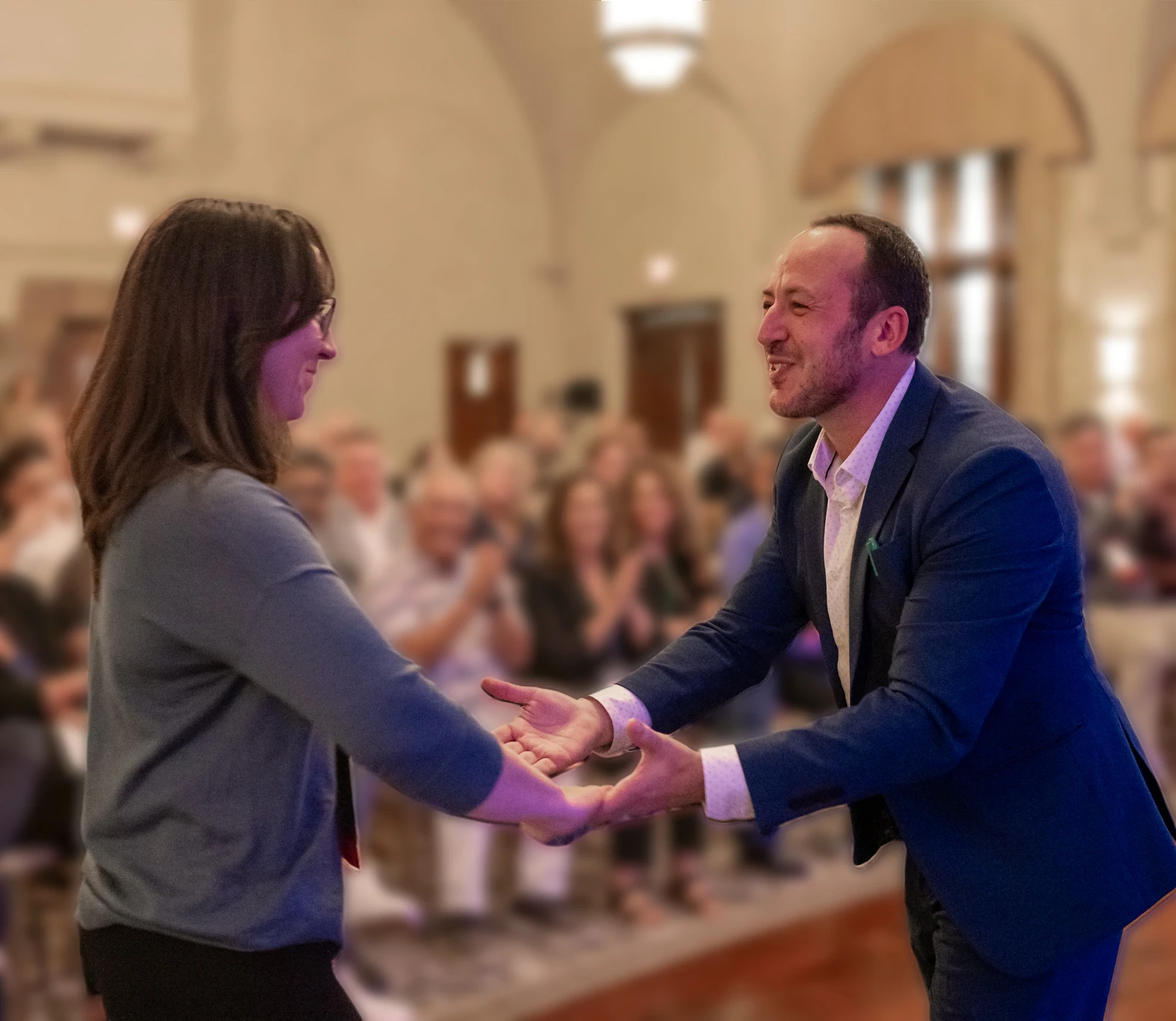 Kostya Kimlat reaching out to welcome a volunteer from the audience as the room applauds