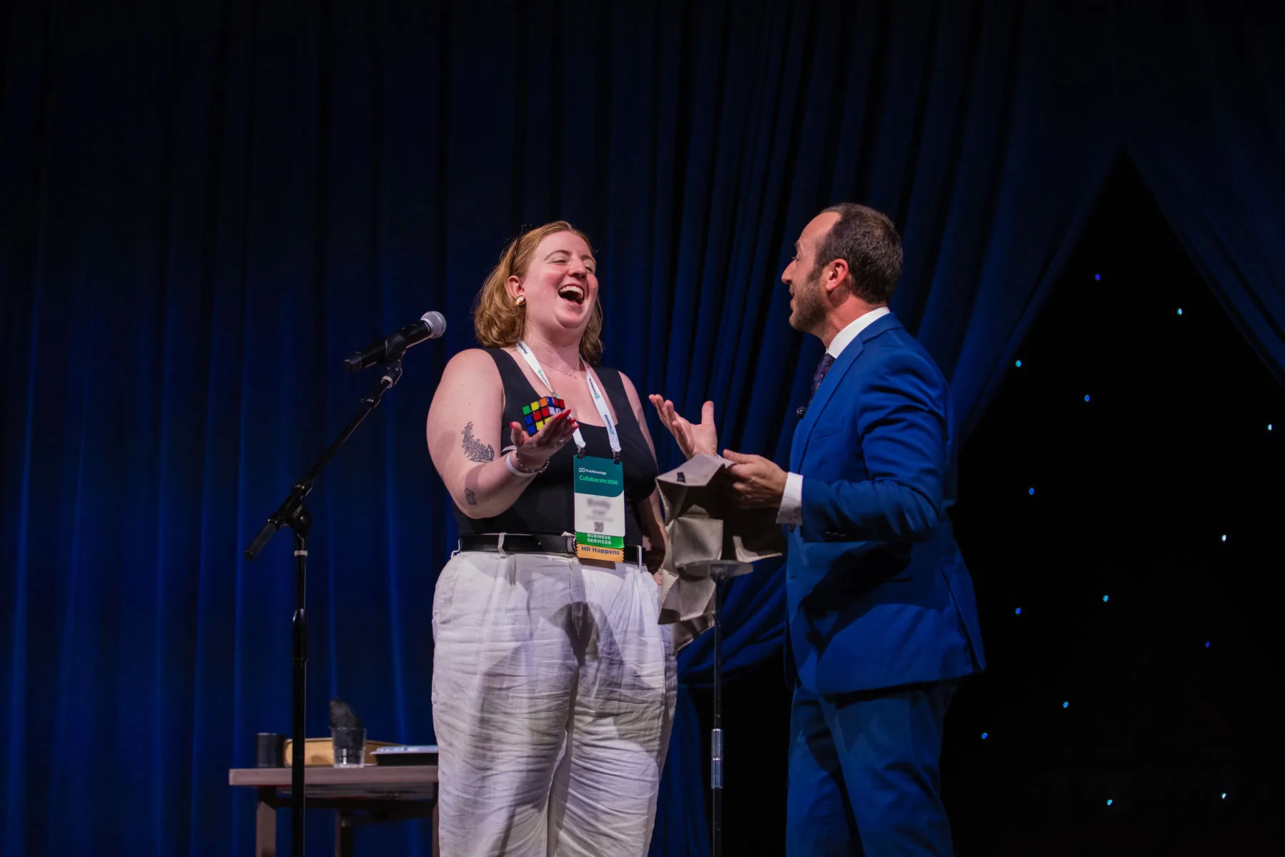 Kostya Kimlat on stage with an audience volunteer who laughs as a Rubik’s Cube appears in her hand