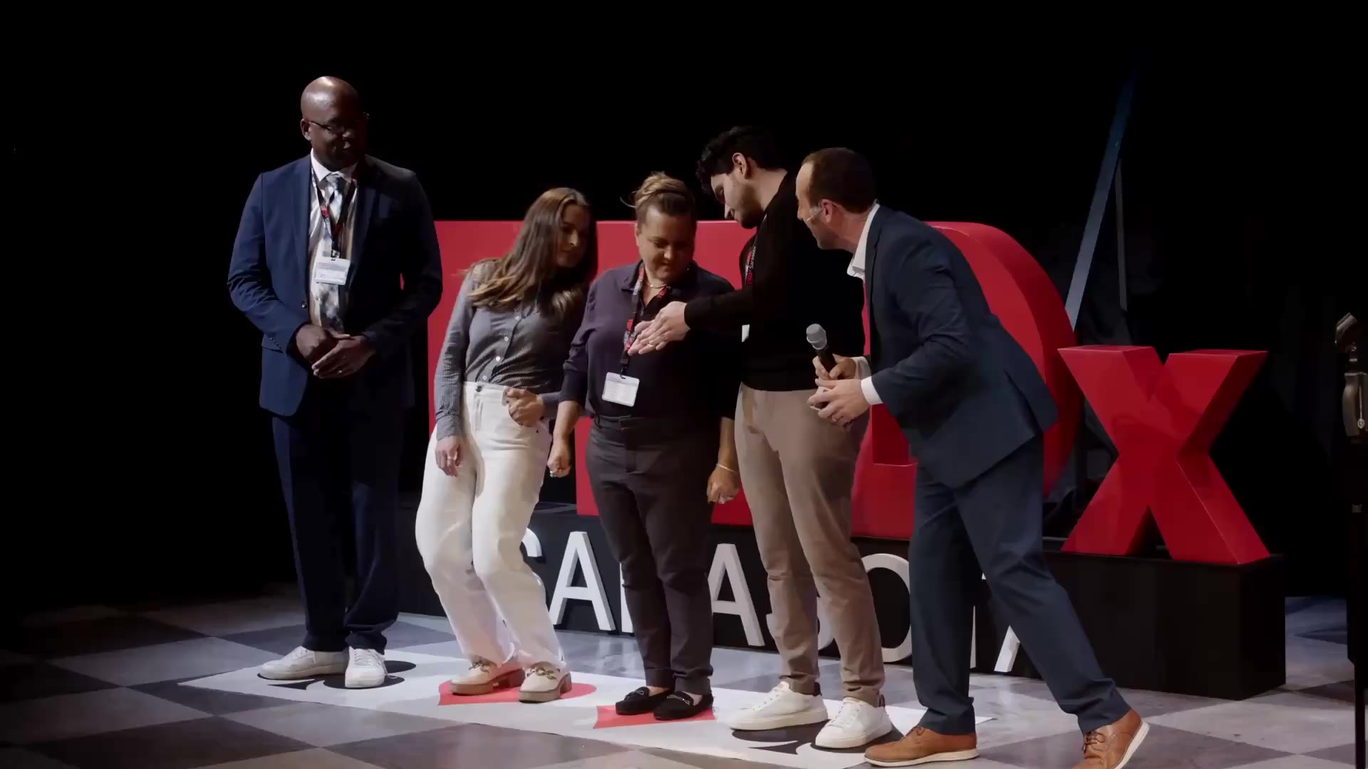 Kostya and four laughing volunteers on the TEDx Sarasota stage, the red TEDx letters behind them